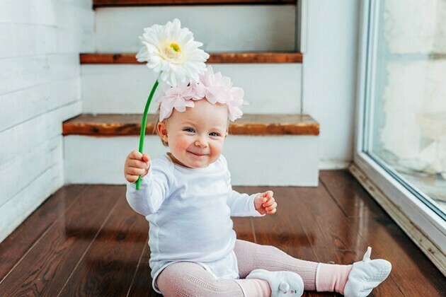 Little baby girl wearing spring wreath siting on floor in bright light living room near window and playing with gerbera flowers | McSwain Carpet & Floors